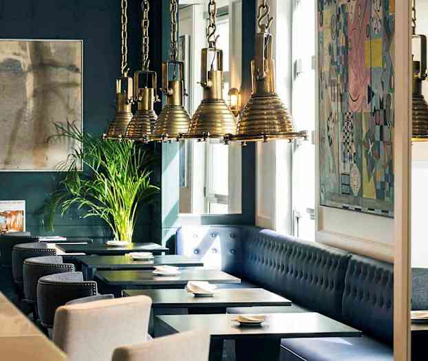 Interiör av en restaurang med mörkblåa väggar, konstverk, hängande lampor och sittplatser vid bord. (AI-genererad text)