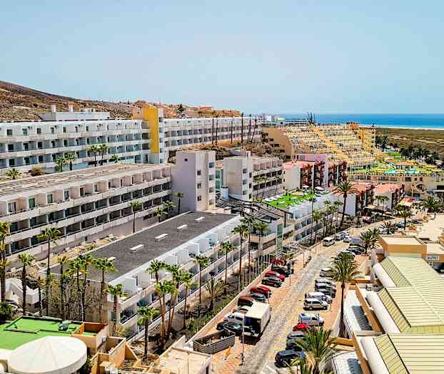 Hotellbyggnader nära havet med parkerade bilar och palmer. (AI-genererad text)