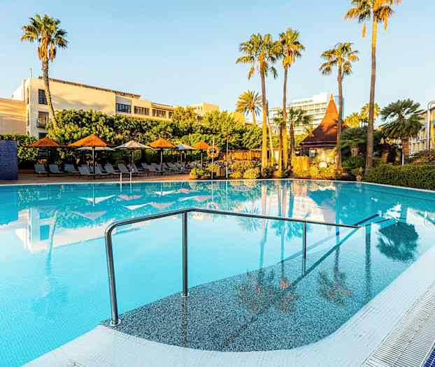 En utomhuspool omgiven av solstolar, parasoller och gröna palmer under en klarblå himmel. (AI-genererad text)