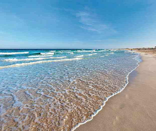 En sandstrand med mjuka vågor som sköljer in, under en klar blå himmel. (AI-genererad text)