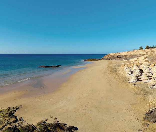 En sandstrand med solstolar och parasoller vid havet. (AI-genererad text)