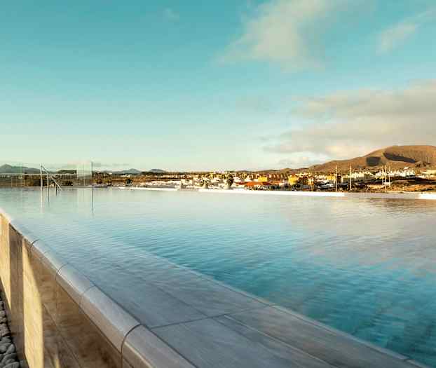 En infinitypool under klar himmel med utsikt över en stad och berg i bakgrunden. (AI-genererad text)
