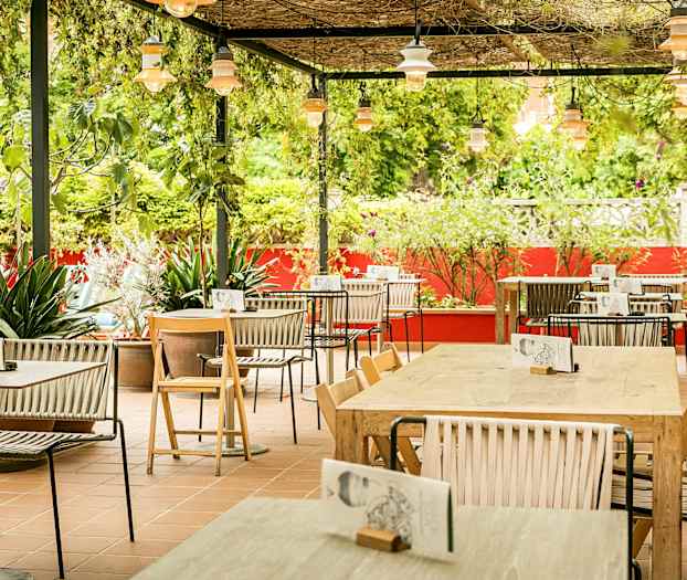 En utomhusservering med bord och stolar, omgiven av grönska och röda väggar. (AI-genererad text)