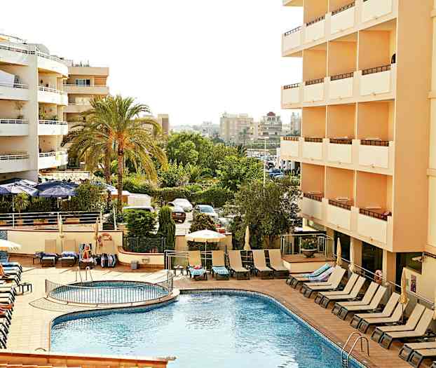 Hotell med utomhuspool och solstolar, omgivna av gröna träd och höghus. (AI-genererad text)