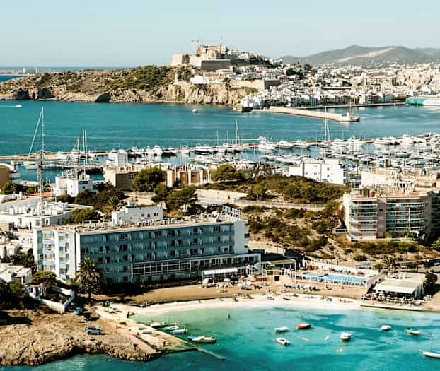 En kuststad med flera byggnader och en småbåtshamn; små båtar och en strand syns i förgrunden. (AI-genererad text)