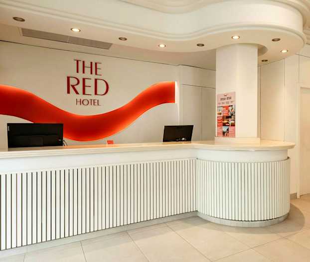 Hotellreception med vit inredning och röd logotyp på väggen. (AI-genererad text)