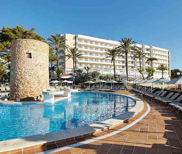 En swimmingpool omgiven av solstolar, med ett stenbyggt torn och ett hotell i bakgrunden. (AI-genererad text)