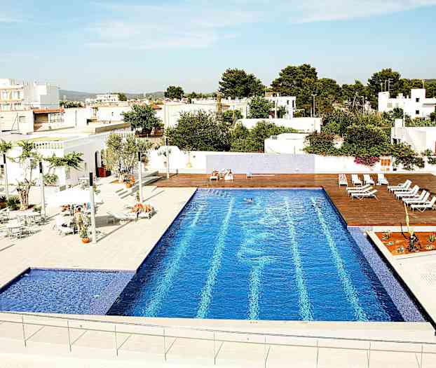 En utomhuspool med blått kakel, omgiven av solstolar och vita byggnader. (AI-genererad text)