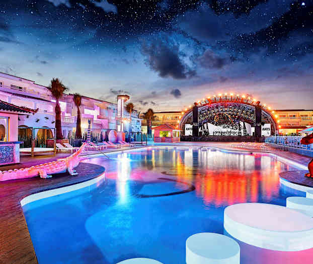 En utomhuspool vid ett upplyst hotellområde under natthimlen. (AI-genererad text)