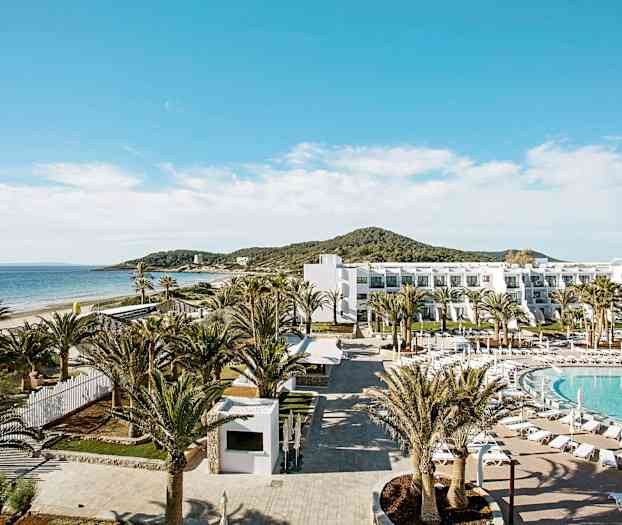 Ett hotellområde vid stranden med pool, palmer och en byggnad i vitt. (AI-genererad text)