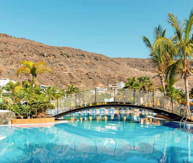 En pool med en bro och palmer omgivna av berg. (AI-genererad text)