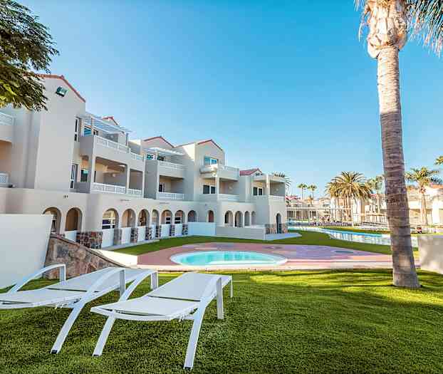 Utomhusområde med solstolar, gräsmatta, pool samt närliggande byggnad i ljusa färger. (AI-genererad text)