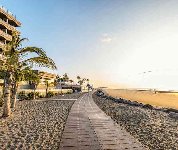 En strandpromenad vid en sandstrand med palmer och byggnader. (AI-genererad text)