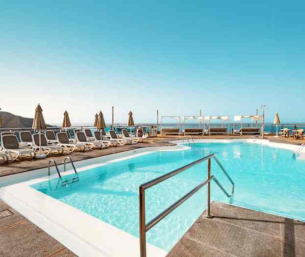 Poolområde med solstolar och parasoller samt utsikt över havet. (AI-genererad text)