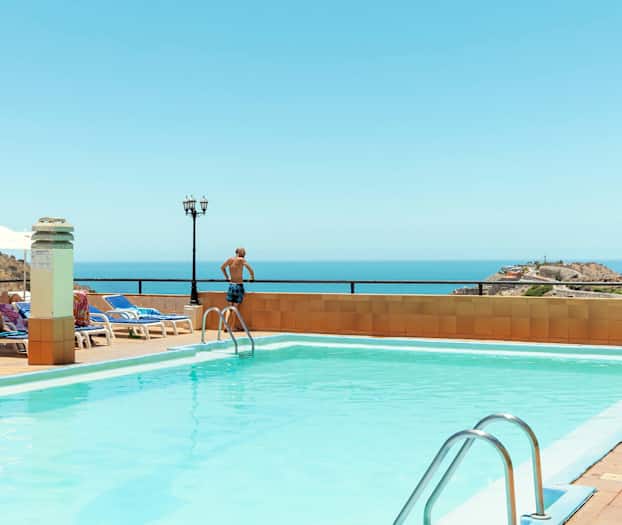 Utomhuspool med havsutsikt, solstolar och parasoller. (AI-genererad text)