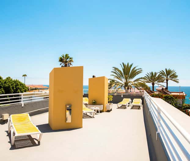 En takterrass med solstolar och utsikt över palmer och hav. (AI-genererad text)