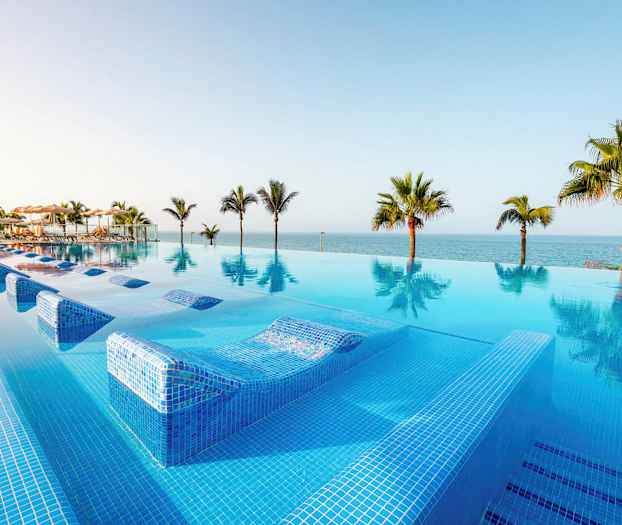 En infinitypool med utsikt över havet och omgivande palmer. (AI-genererad text)