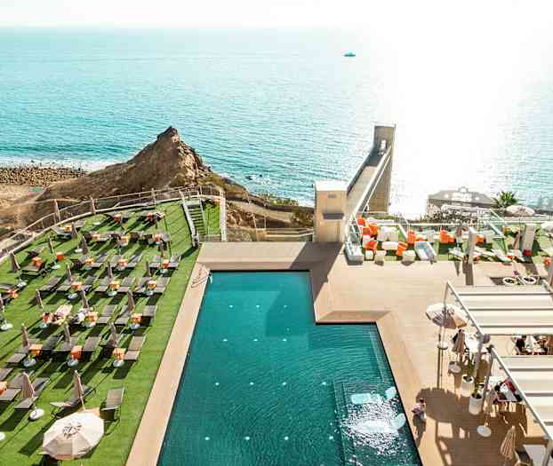 Utsikt över en swimmingpool vid en utomhusterrass med solstolar och havet i bakgrunden. (AI-genererad text)