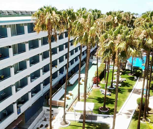 Hotell med vita fasader omgivet av gräsmatta med palmer och en pool. (AI-genererad text)