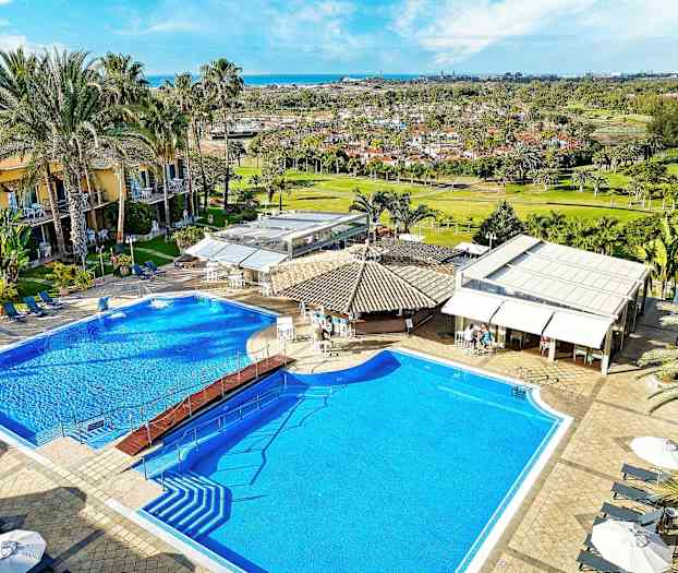 Bild av en hotellpool med solsängar, parasoller och omgivande byggnader. (AI-genererad text)