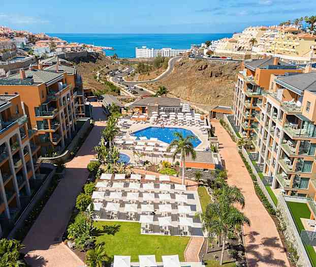 Hotellområde med pool, solstolar och omgivande byggnader, med havet i bakgrunden. (AI-genererad text)