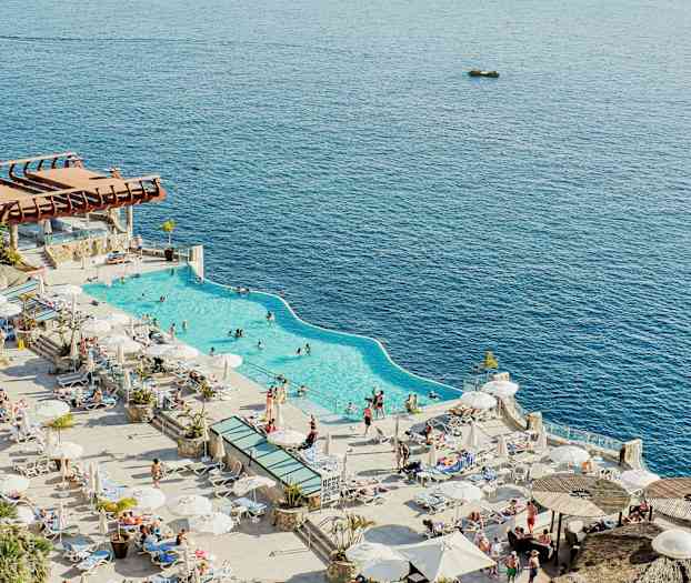 Bild av en strandnära pool med omgivande solsängar och parasoller, mot en bakgrund av havet. (AI-genererad text)