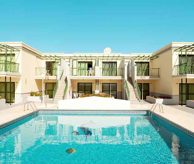 En pool framför en byggnad med balkonger och gröna detaljer. (AI-genererad text)