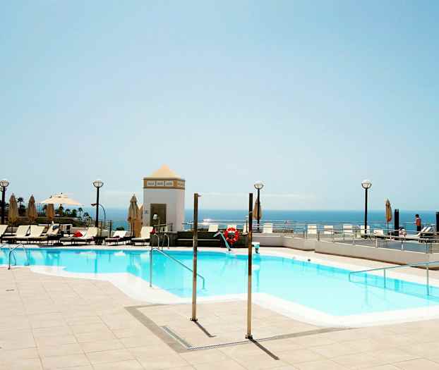 Utomhuspool med solstolar och utsikt över havet. (AI-genererad text)