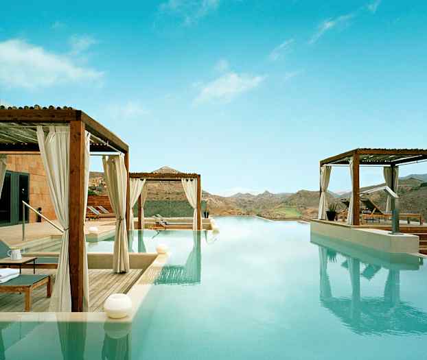 Infinity-pool med utsikt över berglandskapet och omgivande terrasser med solstolar under skärmtak. (AI-genererad text)