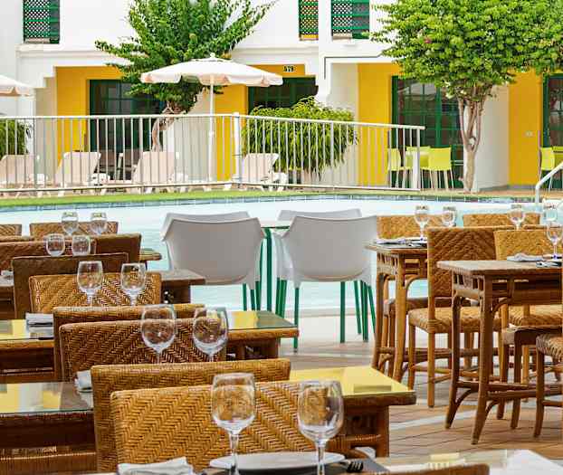 Uteservering med flätade stolar och glasbord nära en pool. (AI-genererad text)