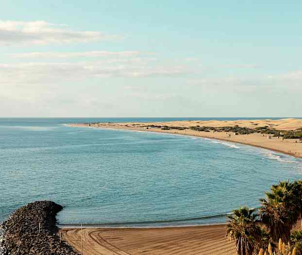 Vy över en strand med sanddyner, hav och en smal stenpir. (AI-genererad text)