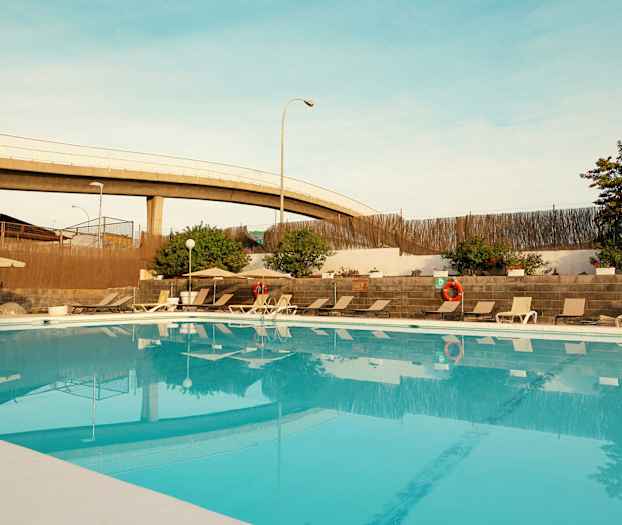 Utomhuspool med solstolar och parasoller, omgiven av växter och mur. (AI-genererad text)