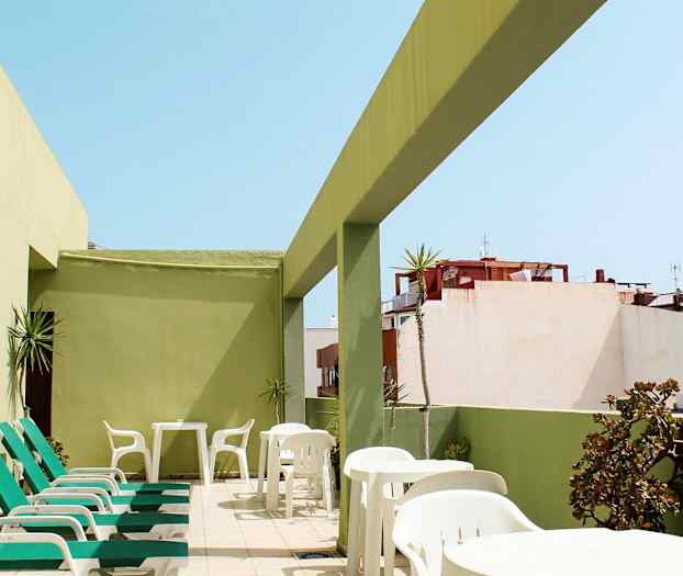 Terrass med solstolar och bord, omgiven av gröna väggar. (AI-genererad text)