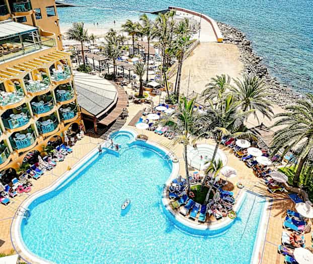 En hotellpool vid kusten med palmer och solstolar runt omkring. (AI-genererad text)