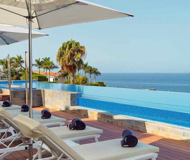 Solstolar och parasoller vid en infinitypool med utsikt över havet. (AI-genererad text)