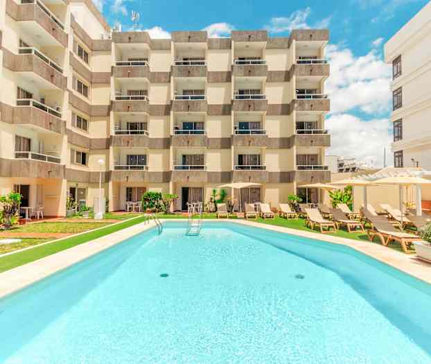 Hotellbyggnad med pool framför. (AI-genererad text)