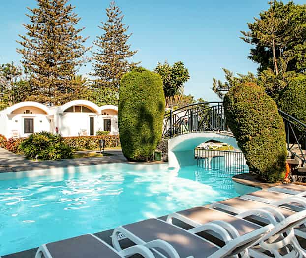 Utomhuspool med spatiös omgivning, solstolar och en liten bro i trädgården. (AI-genererad text)