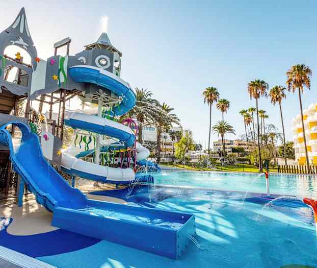 En vattenpark med rutschkanor och lekutrustning, omgiven av palmer och hotellbyggnader. (AI-genererad text)