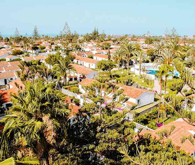 Vy över ett resemål med vita hus, röda tak och gröna träd omkring. (AI-genererad text)