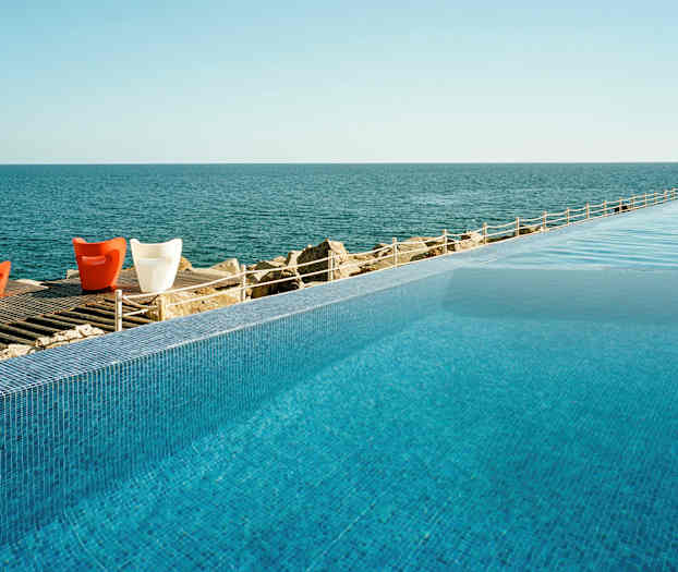 En evighetspool med utsikt över ett lugnt hav och ett trädäck med färgglada stolar. (AI-genererad text)