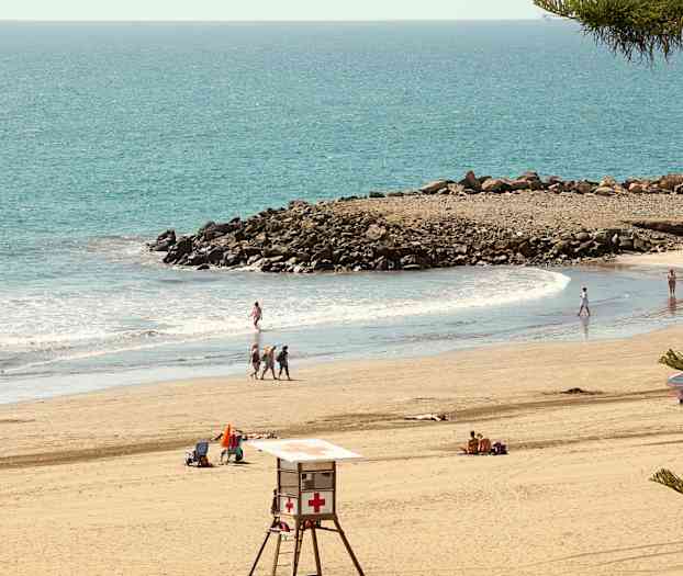 Strand med badgäster, livräddartorn och klippor vid havet. (AI-genererad text)