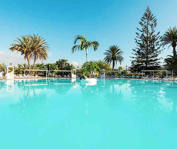 En stor turkos swimmingpool omgiven av solstolar och palmer. (AI-genererad text)