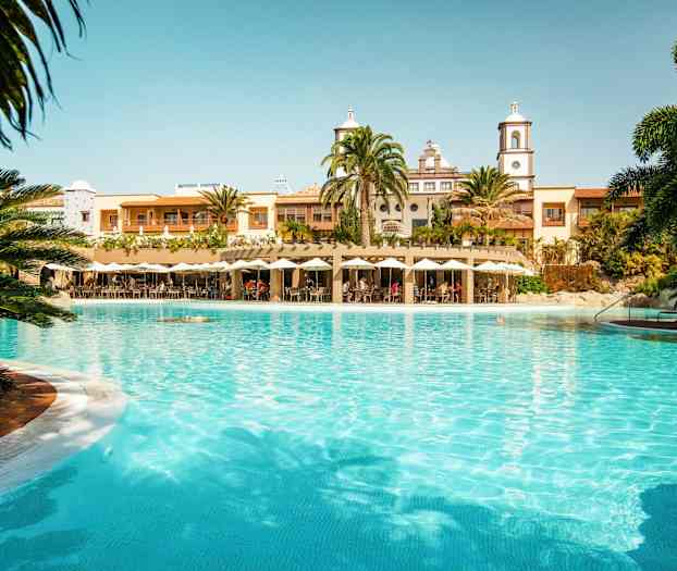 En stor pool framför en byggnad med palmer och parasoller. (AI-genererad text)