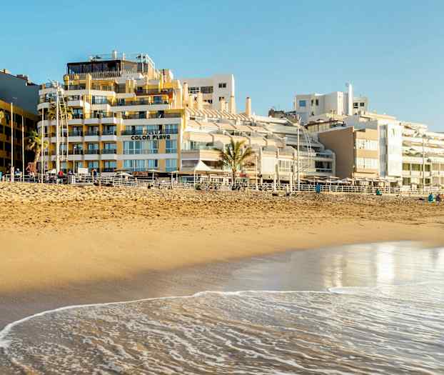 En sandstrand vid havet med byggnader i bakgrunden. (AI-genererad text)