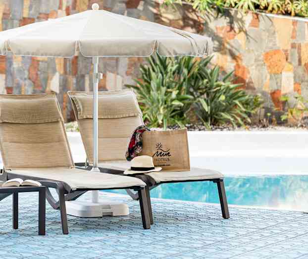 Två solstolar med parasoll vid en pool, med en Juicy motellväska och en hatt. (AI-genererad text)