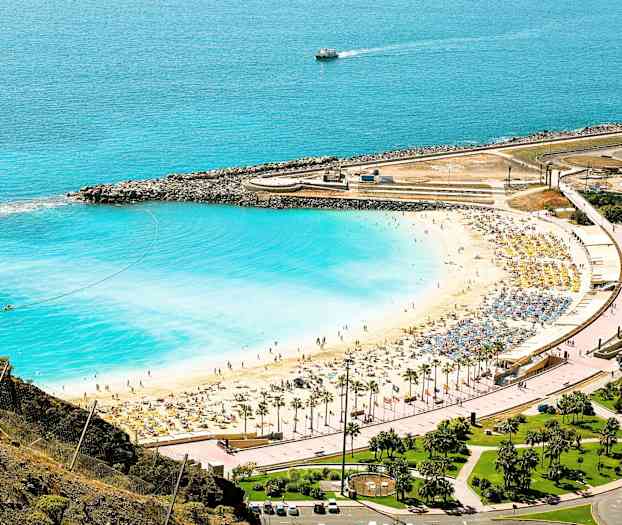 En strand med vit sand och blått vatten vid en kustlinje som har solsängar och parasoller. (AI-genererad text)