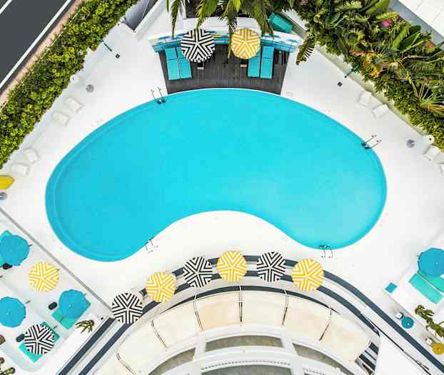 Flygbild på ett poolområde med solstolar och färgade parasoller. (AI-genererad text)