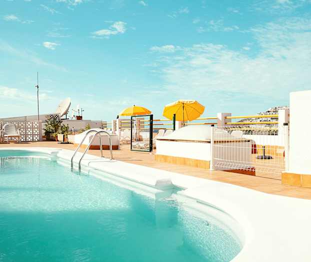 En utomhuspool med turkost vatten omgiven av en solterrass med gula parasoller. (AI-genererad text)