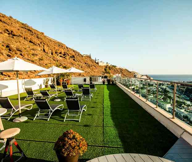 Bild av en terrass med solstolar, parasoller och utsikt över havet och omgivande klippor. (AI-genererad text)