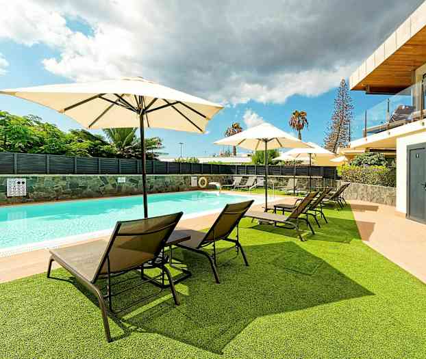 En utomhuspool med solstolar och parasoller på gräs och trädäck. (AI-genererad text)